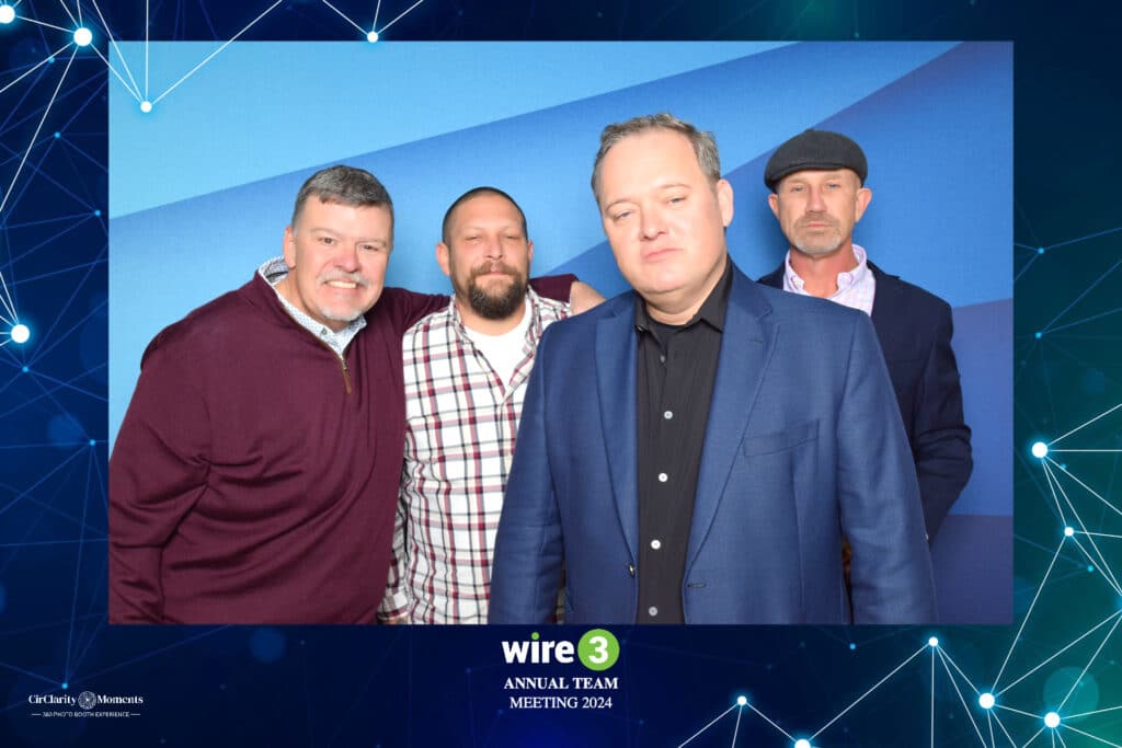 At the Wire3 Annual Team Meeting 2024, four men are captured in front of a blue backdrop, blending casual and business attire with bright smiles. Framed by a blue geometric pattern, this moment is perfectly preserved in the Digital Photo Booth.