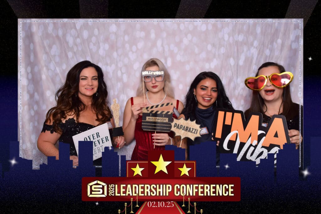 Four people pose at a digital photo booth with fun props like a clapperboard, sunglasses, and signs reading Im a VIP and Paparazzi. A 2025 Leadership Conference banner is prominently displayed below with the date 02.10.25.