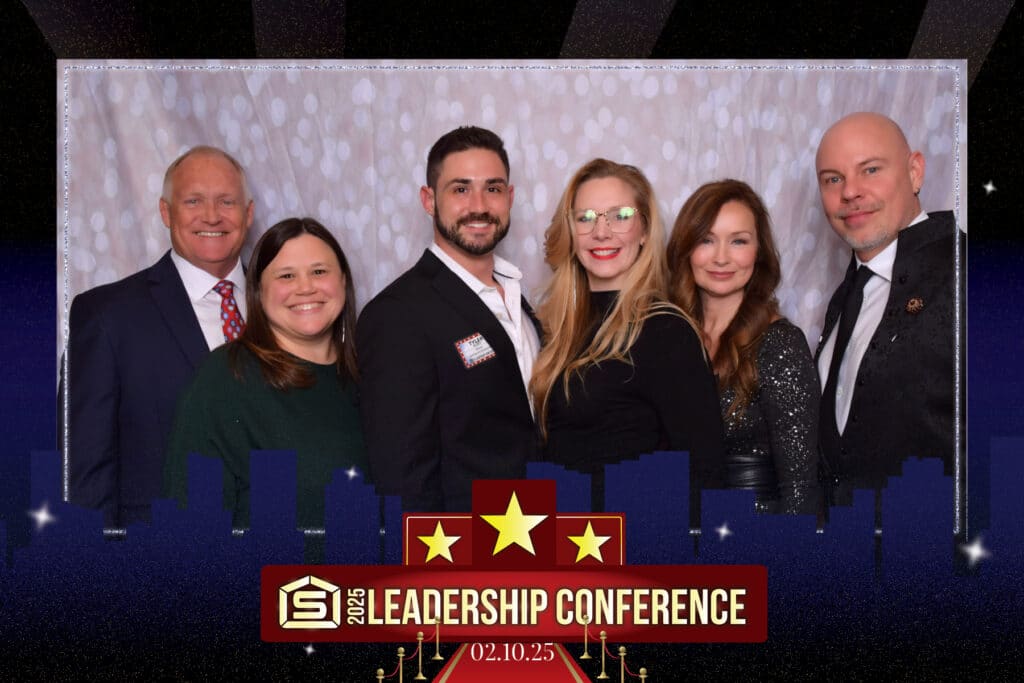 Six people, three men and three women in formal attire, pose against a light, textured backdrop. The frame, designed like a city skyline, is labeled “2025 Leadership Conference” with the date “02.10.25.” It captures the essence of a sophisticated digital photo booth moment.