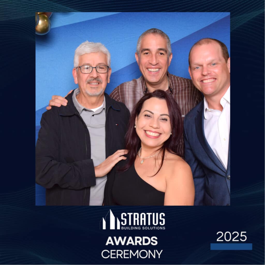 Four people grinning at a digital photo booth, standing against a blue backdrop. This snapshot is from the Stratus Building Solutions 2025 Awards Ceremony, with the event name and year elegantly inscribed at the bottom.