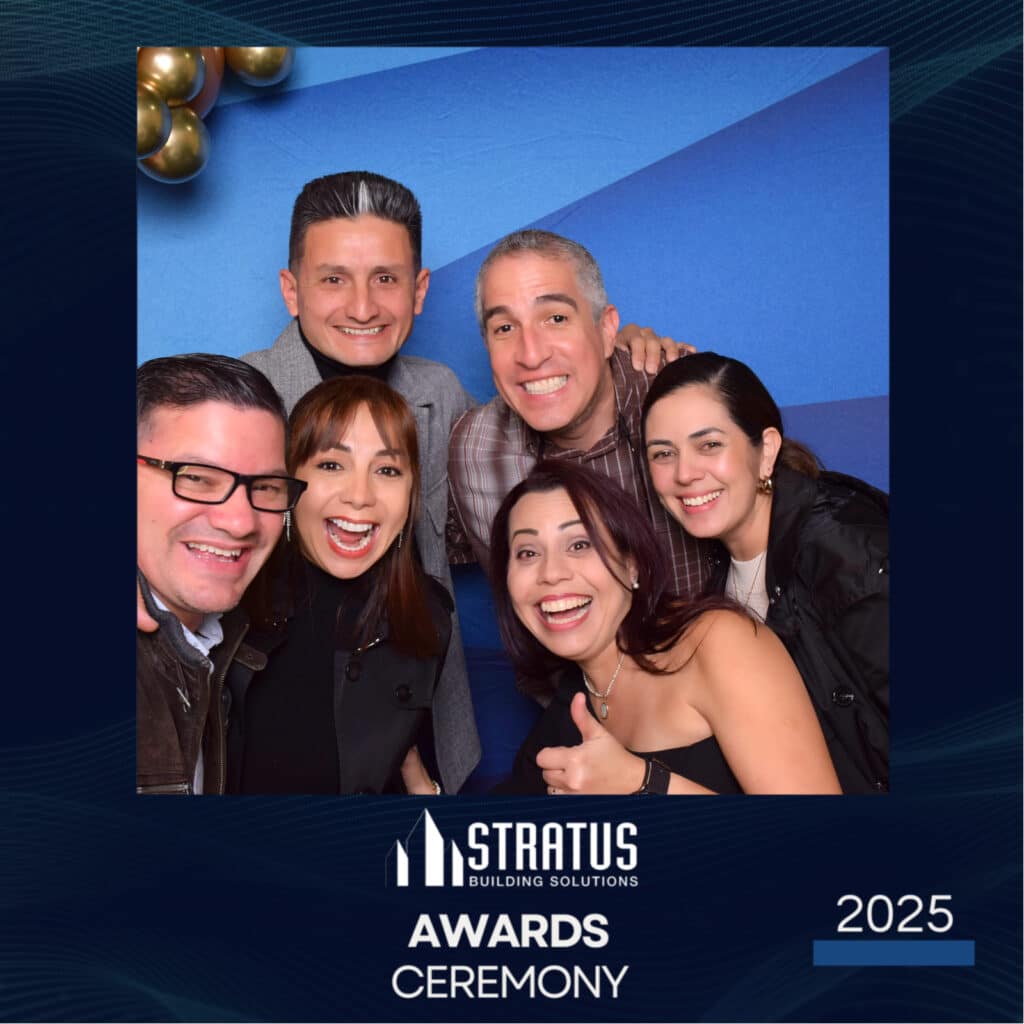 Six smiling people pose together at a Stratus Building Solutions Awards Ceremony 2025. Theyre standing against a blue background with gold balloons in the corner, captured perfectly by the digital photo booth.