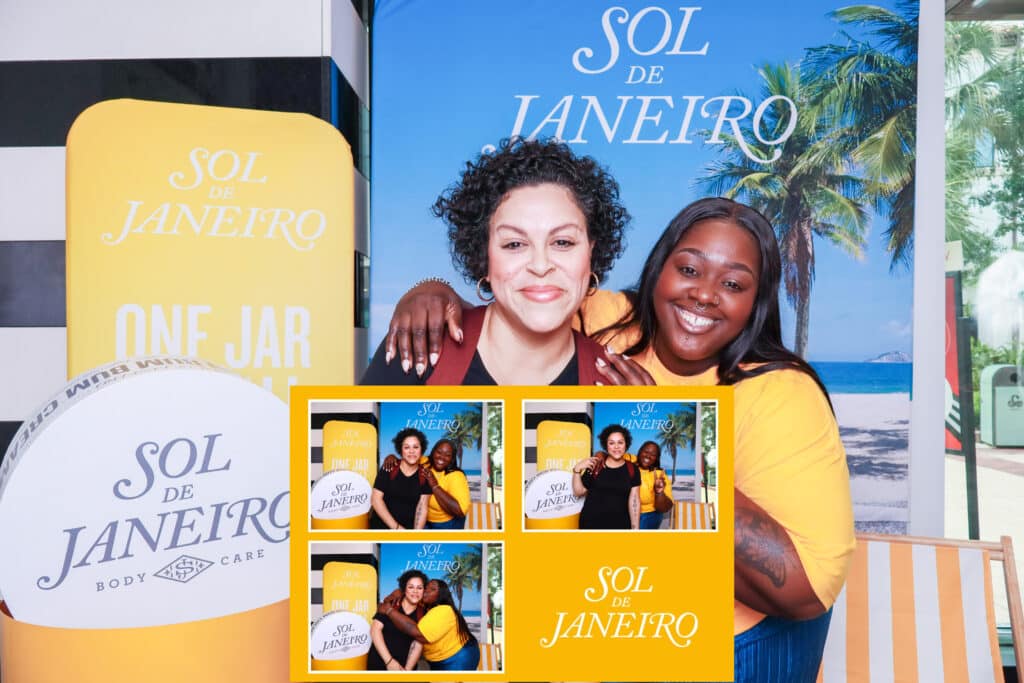 Two women smile and pose together in front of a tropical Sol de Janeiro backdrop, captured by a Digital Photo Booth. Four smaller photos show their fun moments below, along with the Sol de Janeiro logo and body care branding.