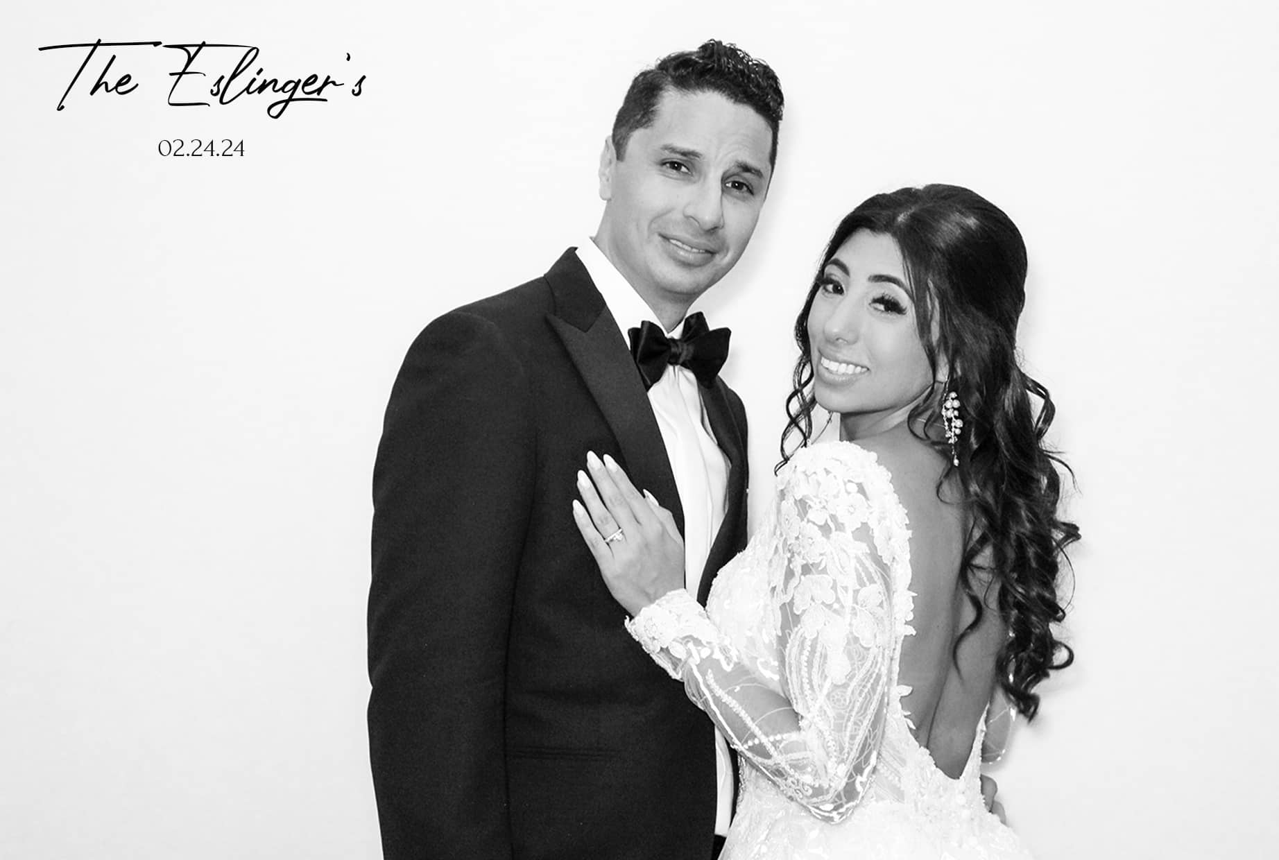 A newlywed couple poses together, smiling. The groom is in a black tuxedo, and the bride is in a lacy white gown with her hair styled in loose curls. The Edingers 02.24.24 is written at the top left. They stand against a plain white background. A newlywed couple poses together, smiling. The groom is in a black tuxedo, and the bride is in a lacy white gown with her hair styled in loose curls. The Edingers 02.24.24 is written at the top left. They stand against a plain white background.