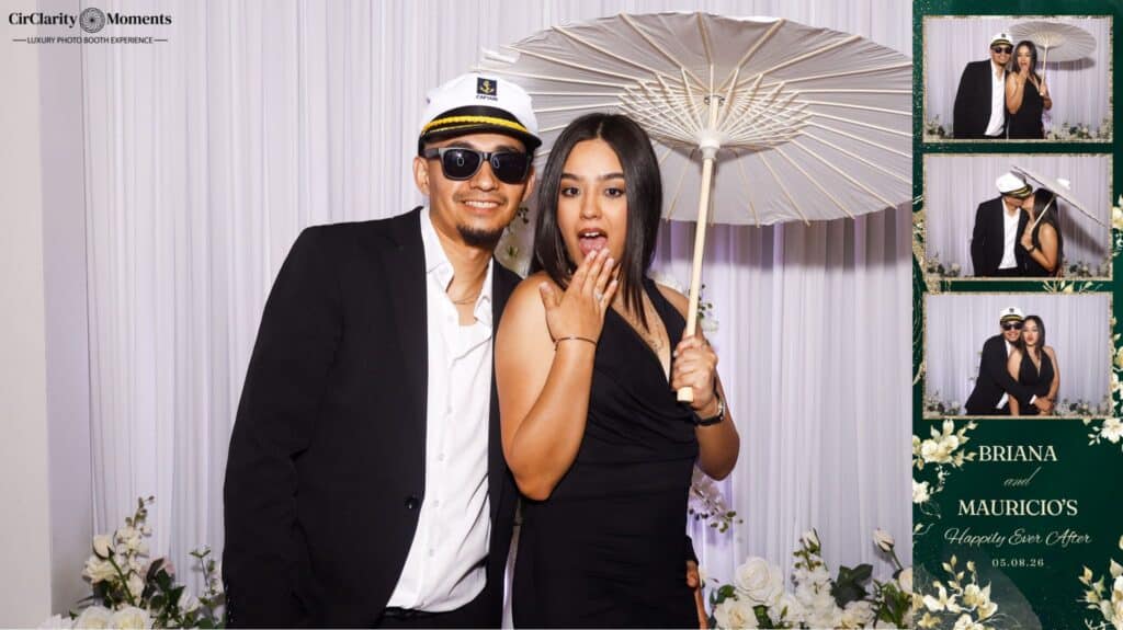 A man in a suit and captain&rsquo;s hat and a woman in a black dress holding a white parasol pose playfully in front of a white curtain backdrop. On the right, a Digital Photo Booth strip shows off their fun poses.