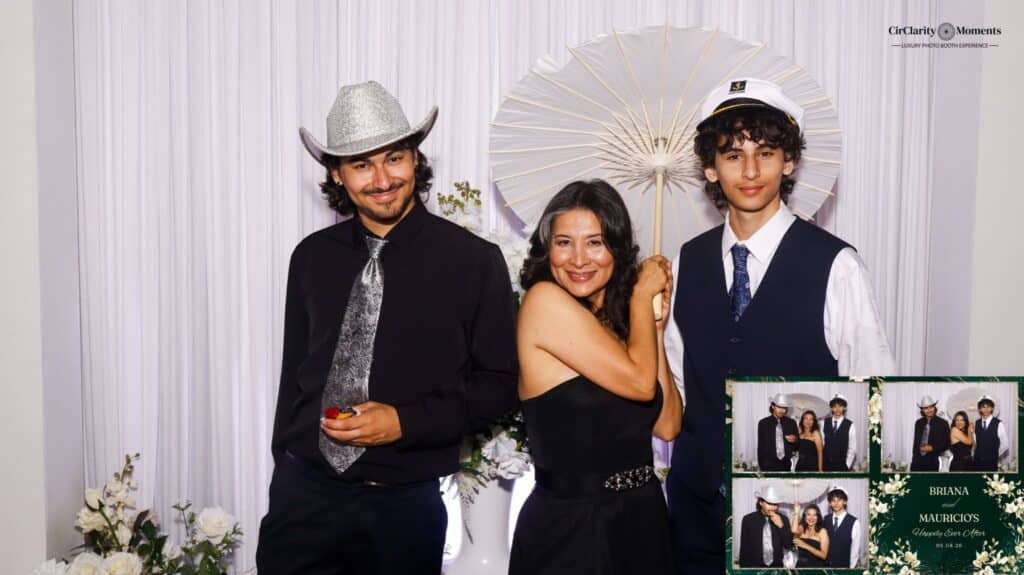 Three people pose for a Digital Photo Booth picture: a man in a silver cowboy hat, a woman with a white parasol, and a young man in a captain&rsquo;s hat and vest. Flowers and small photo strips are visible in the foreground.