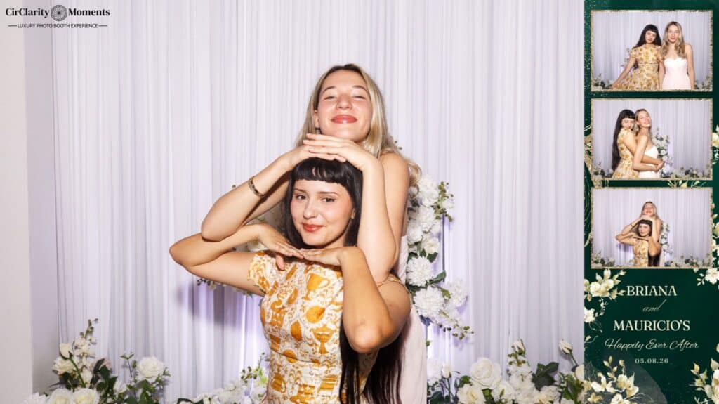 Two women pose playfully in front of white curtains and floral arrangements, captured by a Digital Photo Booth; one stands behind the other with her arms around her shoulders. On the right, a photo strip shows more poses and &ldquo;Briana and Mauricio&rsquo;s Happily Ever After.&rdquo;.