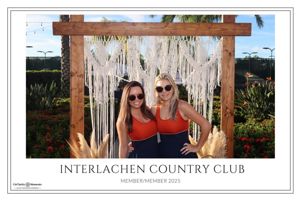 Two women wearing matching outfits pose and smile in front of a decorative wooden arch with macram&eacute;, plants, and a Digital Photo Booth at Interlachen Country Club. Text reads: Interlachen Country Club Member/Member 2025.